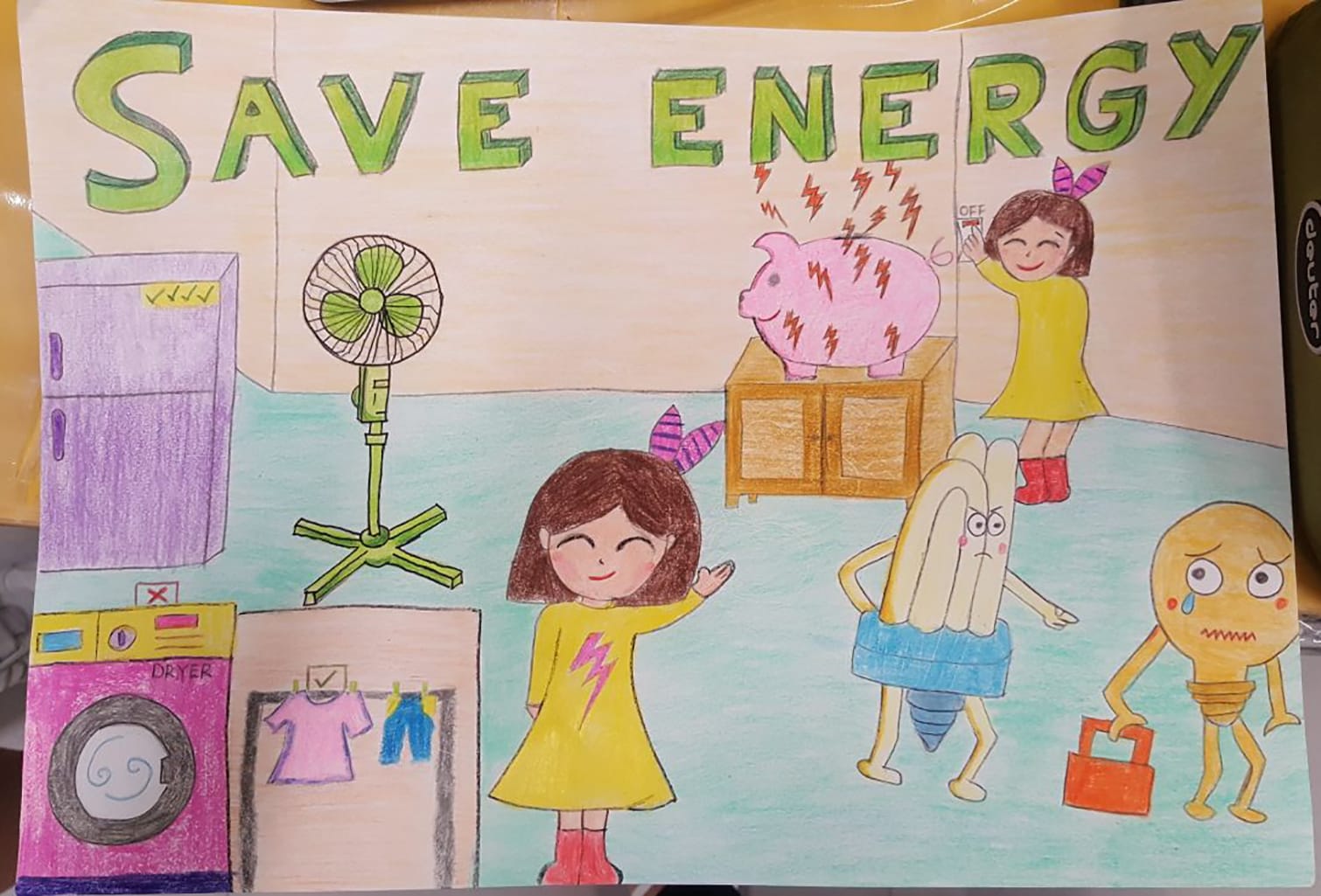 A hand-drawn poster reading Save Energy showing two girls, a fan, appliances, a piggy bank, and cartoon bulb characters.